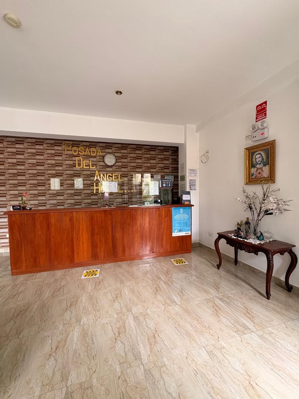 A reception desk with a wooden panel design, a framed picture above it, and a small table with a vase to the right.