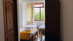 Een hotelkamer met twee bedden, een raam met gordijnen en een houten deur.
