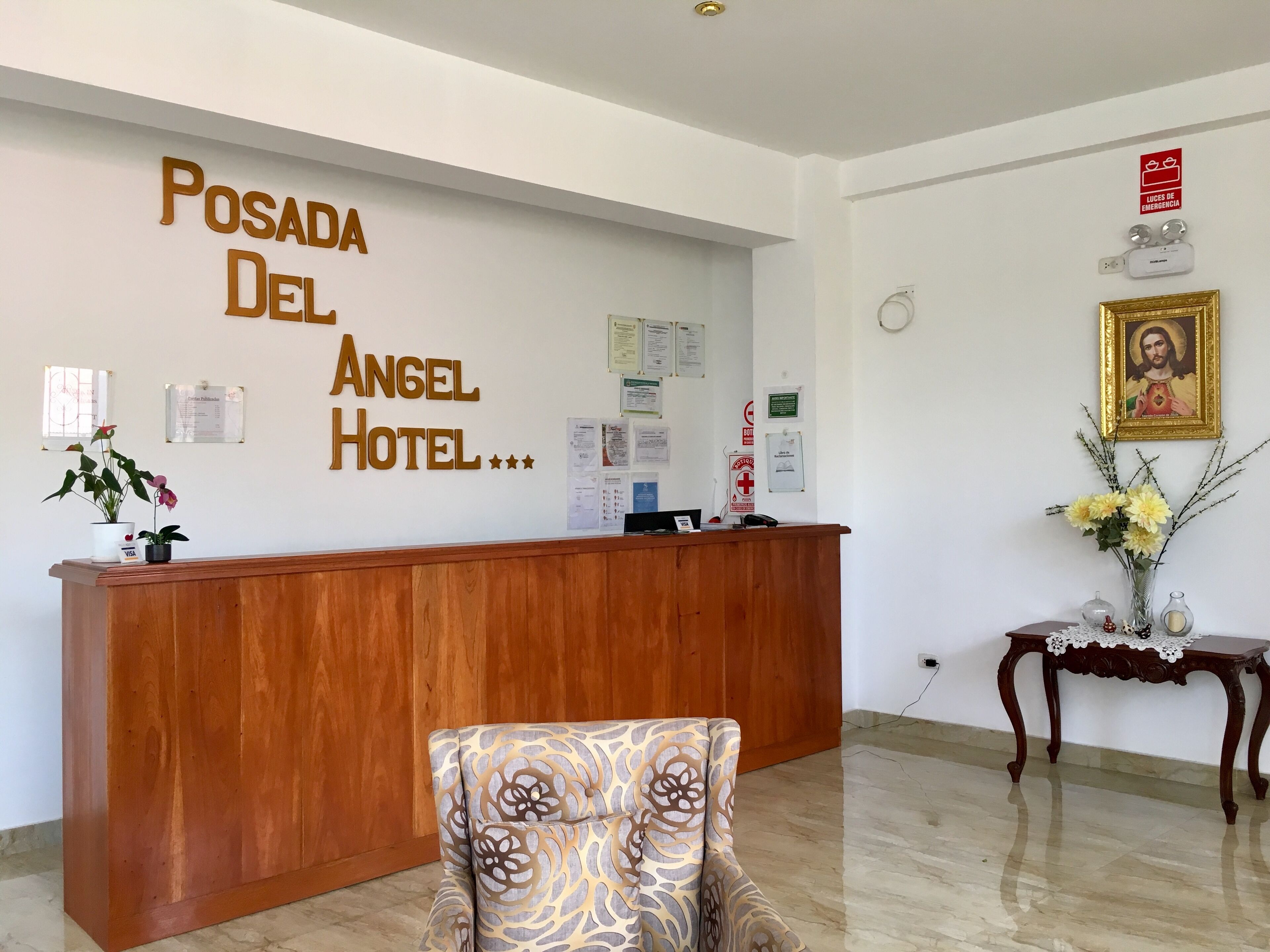 Una recepción con detalles de madera, un letrero en la pared que dice "Posada Del Angel Hotel" y un arreglo floral sobre una mesita.