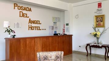 Una recepción con detalles de madera, un letrero en la pared que dice "Posada Del Angel Hotel" y un arreglo floral sobre una mesita.