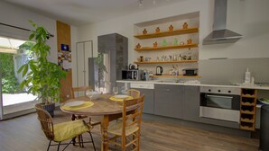 A modern kitchen with a dining area, wooden chairs, a potted plant, and built-in shelves with kitchenware.