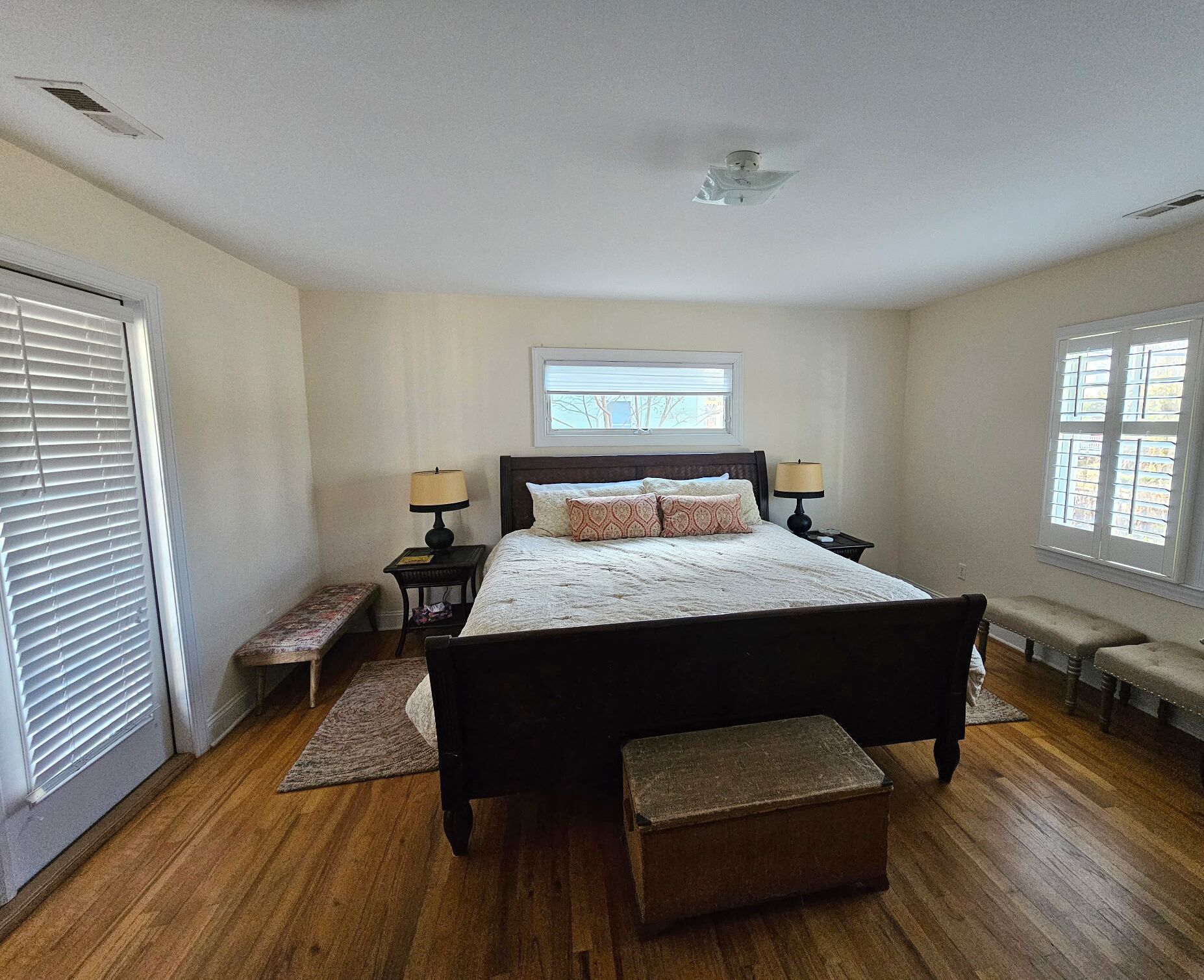A bedroom with a large bed, two bedside tables with lamps, a bench, a window, and a ceiling fan.