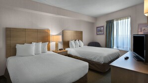 Ein Hotelzimmer mit zwei Betten, einem Schreibtisch mit Fernseher und einem Fenster mit Vorhängen.