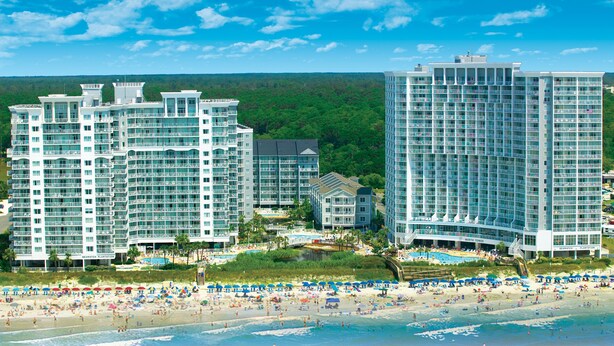 Ein Hotelkomplex direkt am Strand mit mehreren Hochhäusern, einem Poolbereich und einem Strand mit Sonnenschirmen.