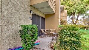 An outdoor seating area with a small table and two chairs, a potted plant, and a building entrance with a door and a number sign. - Scottsdale Chic Condo w/ Heated Pool, Walk Everywhere! A+ LUXURY in Old Town (Scottsdale)