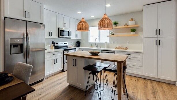 A modern kitchen with white cabinets, stainless steel appliances, a wooden island with stools, and pendant lighting. - Scottsdale Chic Condo w/ Heated Pool, Walk Everywhere! A+ LUXURY in Old Town (Scottsdale)