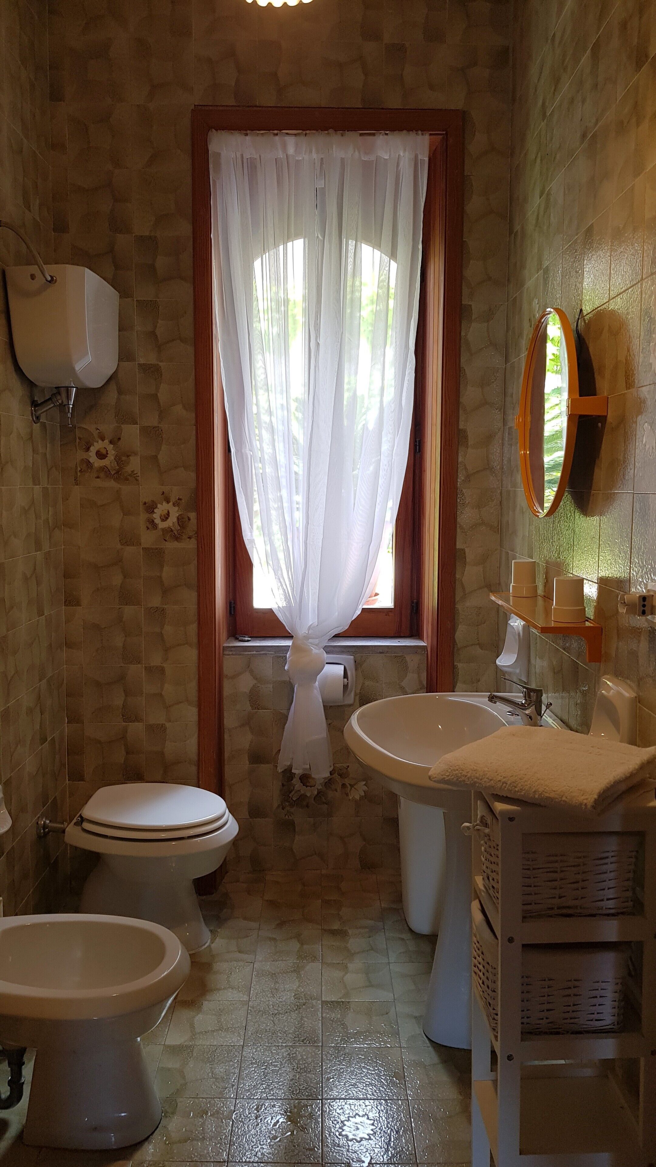Un baño con dos inodoros, un lavamanos, un espejo y una ventana con cortina.