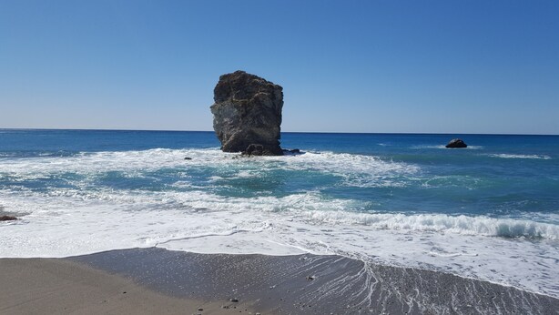 Una playa con una destacada formación rocosa en el agua y una orilla arenosa.