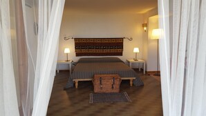 Un dormitorio con una cama, dos mesitas de noche, dos lámparas, un tapiz estampado, una cesta de mimbre y una alfombra.