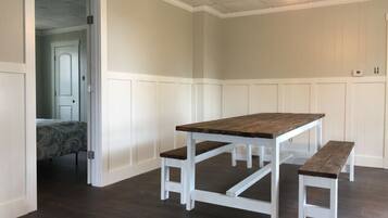 A room with a wooden dining table and benches, white paneled walls, and a dark wooden floor.