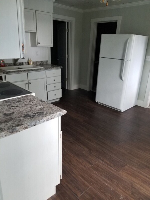 Eine Küche mit weißen Schränken, einer Granitarbeitsplatte, einem weißen Kühlschrank und dunklem Holzboden.
