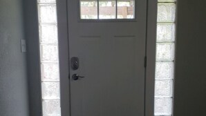 Une porte blanche surmontée d’une petite fenêtre, et flanquée de panneaux en verre dépoli.