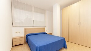 A bedroom with a bed, a nightstand, a wardrobe, and a window with blinds. - Ermitana 2º-B (Peñiscola)