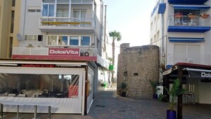 A street with a DolceVita store, a stone building, and a potted plant. - Ermitana 2º-B (Peñiscola)