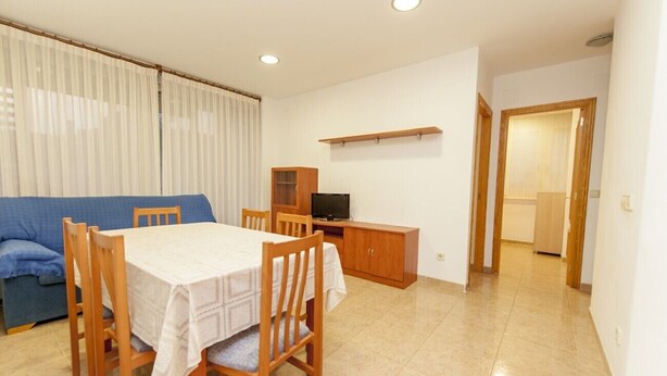A dining area with a table and chairs, a television, and a cabinet. - Ermitana 2º-B (Peñiscola)