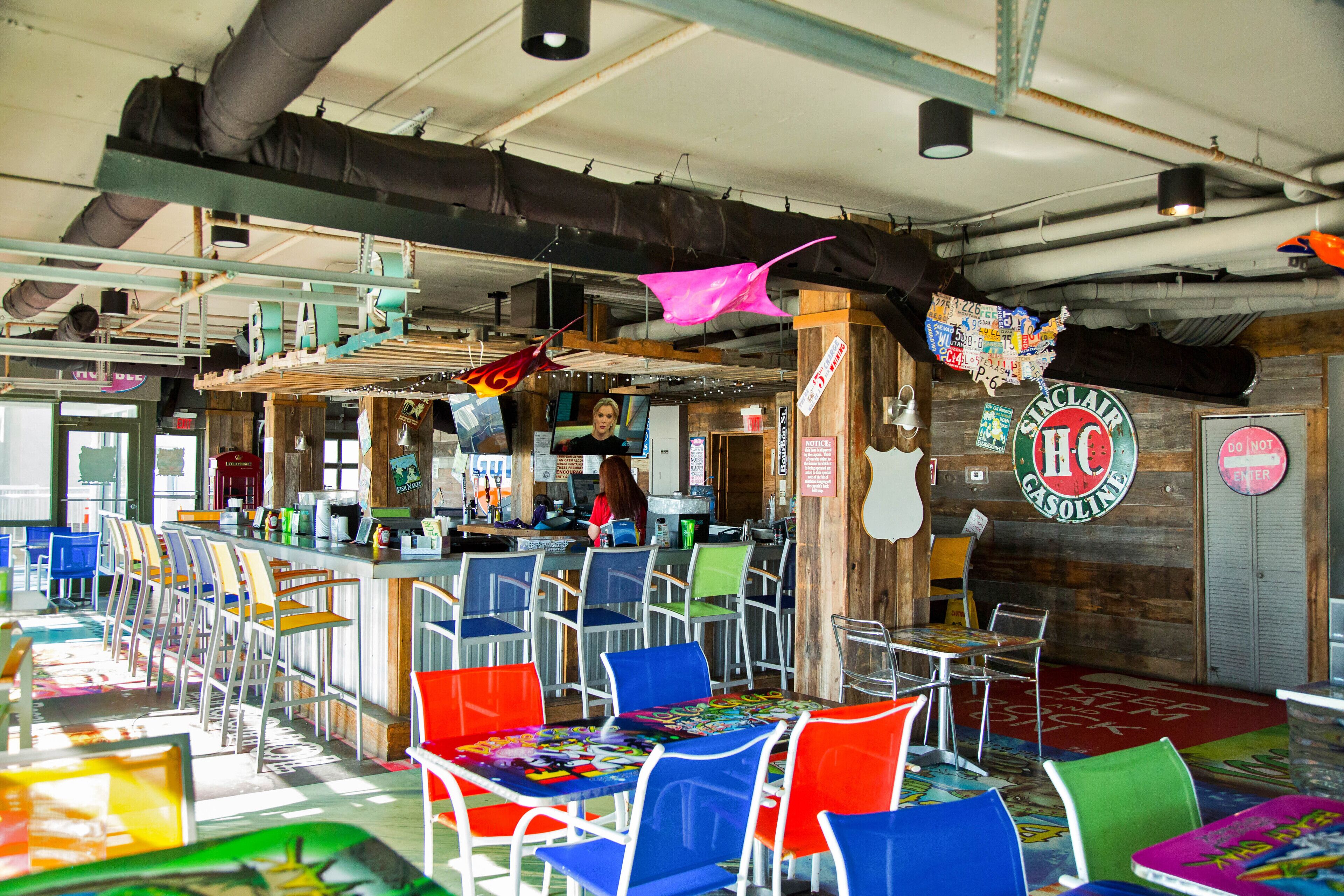 A restaurant with colorful chairs, a bar area, and a wooden wall with a Sinclair sign.