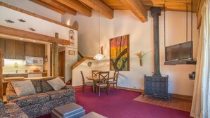 Ein gemütliches Wohnzimmer mit einer Couch, Poufs, einem Esstisch mit Stühlen, einem Kamin und einer Küchenzeile inklusive Mikrowelle und Schränken.
