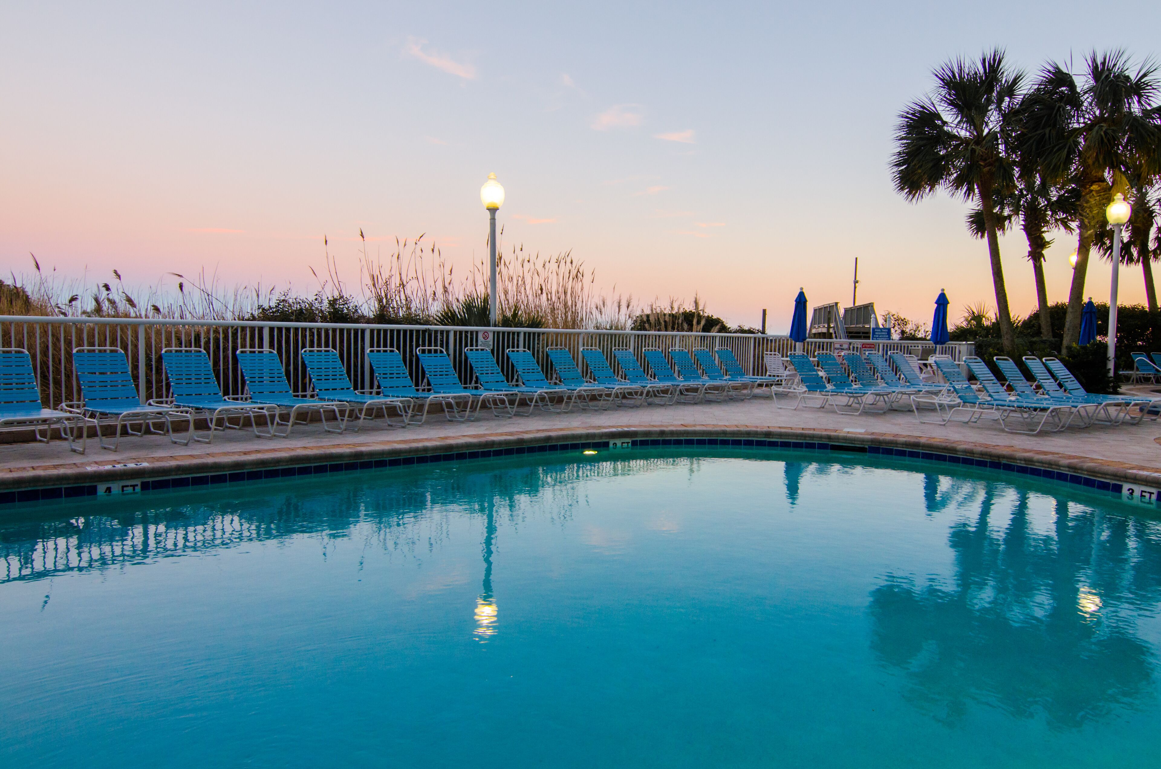 A pool with blue lounge chairs and palm trees in the background.