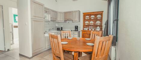 Cocina compacta con armarios blancos, una mesa de madera con sillas y una cafetera.