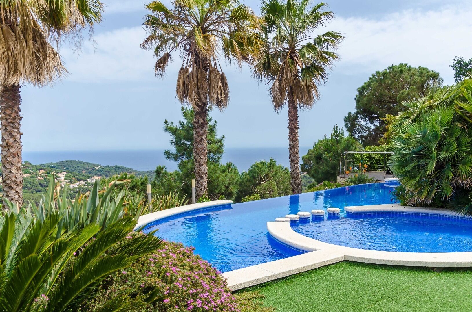 Ein geschwungener Infinity-Pool mit freiem Blick auf den Ozean, umgeben von Palmen und üppiger Vegetation.