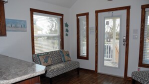 A room with a wooden floor, a sofa with patterned cushions, a bench, and a door with a window. - White Oak -Beautiful Cottage - Perfect For a  Family Getaway (Aransas Pass)