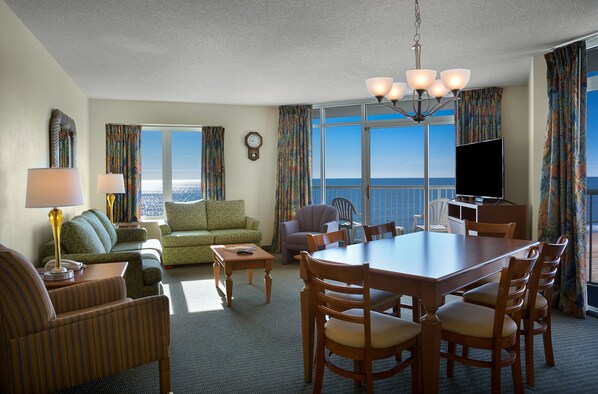 Habitación de hotel con comedor, sofá, televisor y vista al océano.