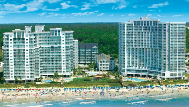 Ein Hotelkomplex direkt am Strand mit mehreren Hochhäusern, einem Poolbereich und einem Strand mit Sonnenschirmen.