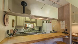 Una cocina con encimera de madera, pileta de acero inoxidable y refrigerador. Hay dos taburetes de madera y un reloj en la pared.