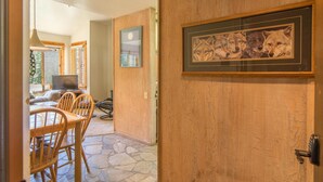 Una puerta de madera con un cuadro enmarcado de lobos, suelo de piedra y una zona de comedor con sillas y una mesa.
