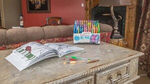 Una mesa de mármol con un libro abierto, bolígrafos y una caja de bolígrafos de gel en una habitación con un sofá y una chimenea.