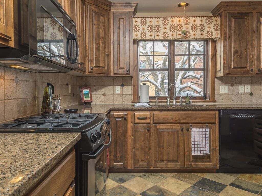 A kitchen with wooden cabinets, a stove, a dishwasher, and a window with a view of trees.