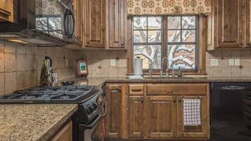 A kitchen with wooden cabinets, a stove, a dishwasher, and a window with a view of trees.