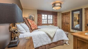 Un dormitorio con cama, mesita de noche, lámpara, escritorio de madera, espejo y ventana con cortinas.