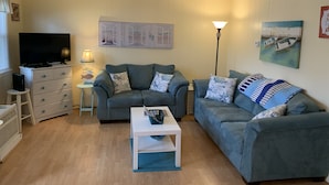 Ett vardagsrum med två grå soffor, ett vitt soffbord, en tv på ett vitt skåp och en lampa.