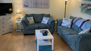 Ett vardagsrum med två grå soffor, ett vitt soffbord, en tv och en lampa.