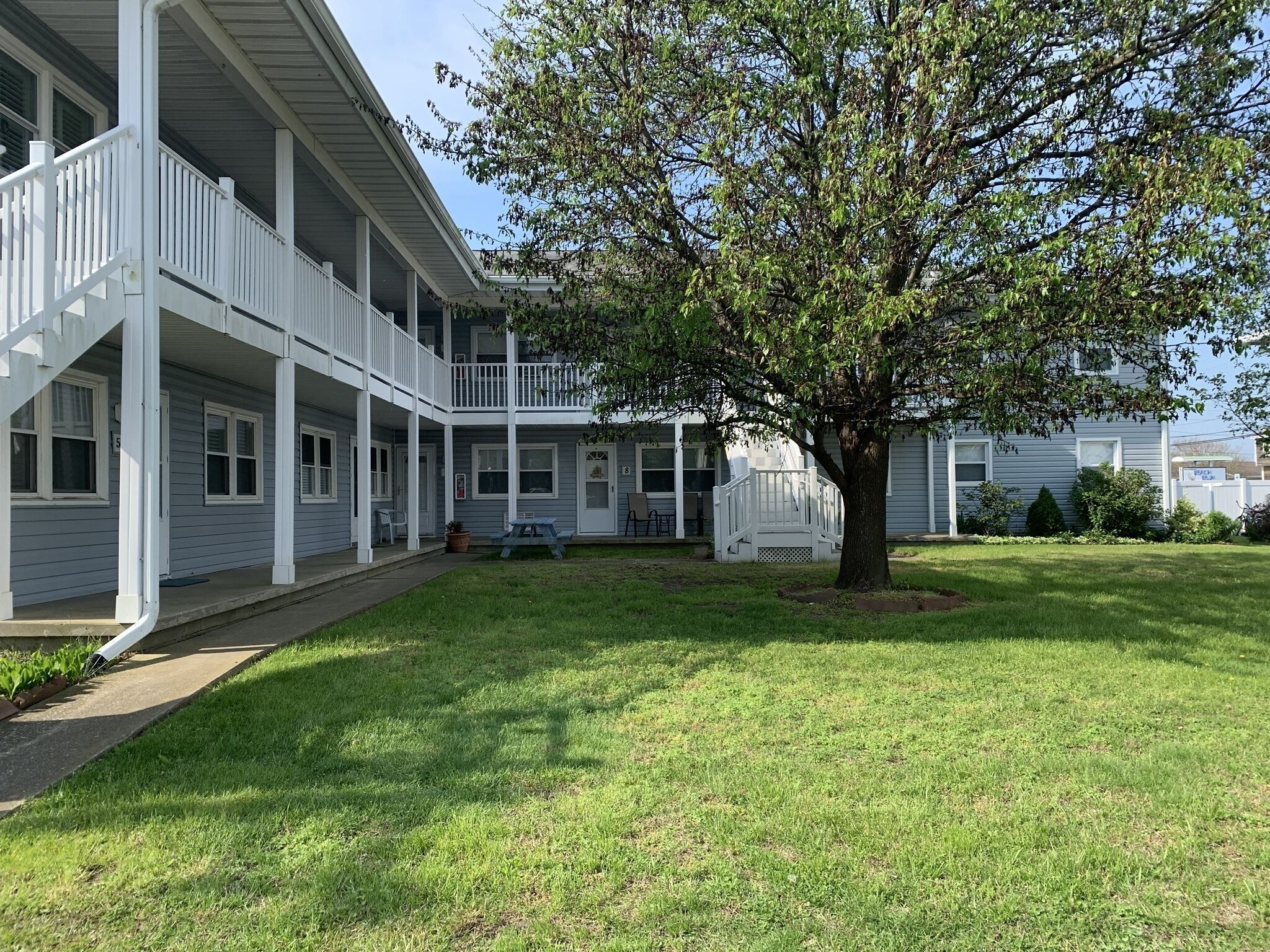 A two-story building with a covered porch and a tree in the yard.