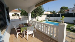 Eine überdachte Terrasse mit Tisch und Stühlen, ein Schwimmbad und Blick auf die umliegende Nachbarschaft.
