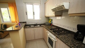 Eine Küche mit Gasherd, Backofen, Spüle und einem Fenster mit Vorhängen.