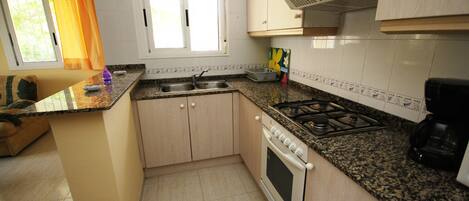 A kitchen with a gas stove, oven, sink, and a window with curtains.