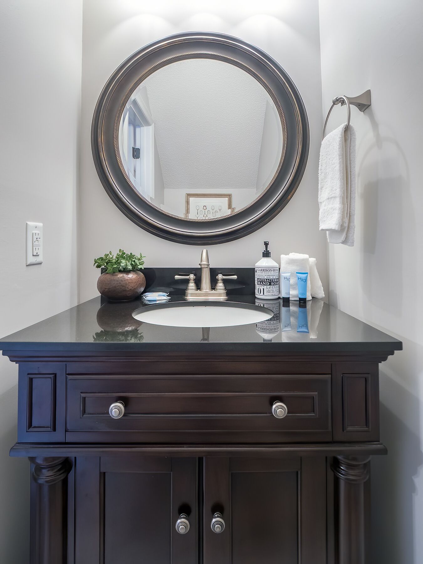 A bathroom vanity with a dark wood finish, a round mirror, and a white sink.