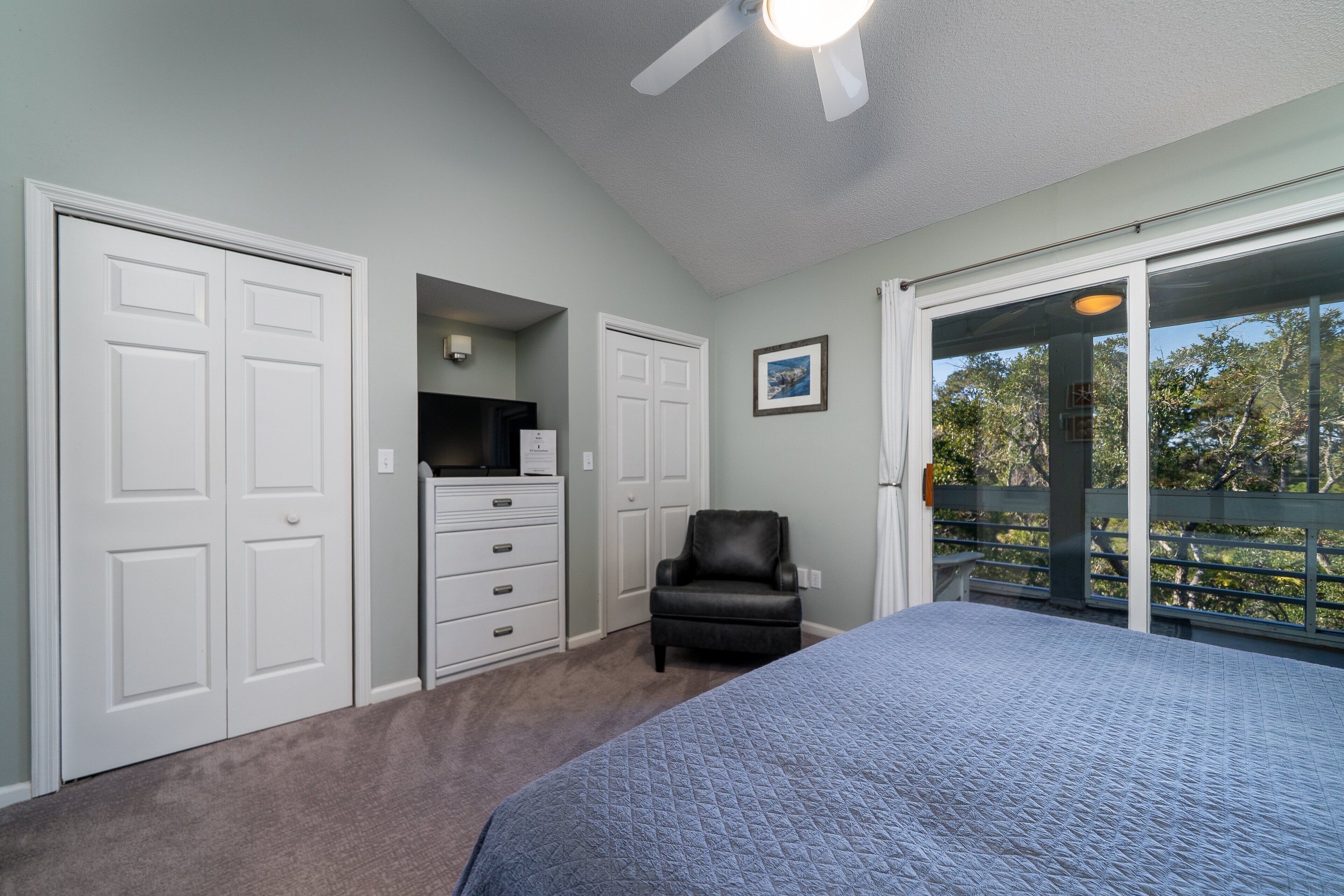 Un dormitorio con cama, cómoda, sillón de cuero negro y ventilador de techo.