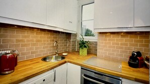 A kitchen with a wooden countertop, a stainless steel sink, a red kettle, and a microwave. - PORTE MAILLOT & ETOILE - PERFECT WORK & TOURIST LOCATION - LUX RENOVATED FLAT (Paris-16)