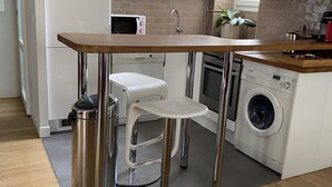 A compact kitchen with white cabinets, a wooden countertop, a built-in washing machine, and a stainless steel trash can. - PORTE MAILLOT & ETOILE - PERFECT WORK & TOURIST LOCATION - LUX RENOVATED FLAT (Paris-16)