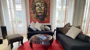 A living room with a black sofa, a round coffee table, and a red rug. There is a large painting on the wall and a window with curtains. - PORTE MAILLOT & ETOILE - PERFECT WORK & TOURIST LOCATION - LUX RENOVATED FLAT (Paris-16)