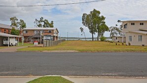 A residential street with houses, a covered parking area, and a grassy area with trees. - Hami's Retreat - Burrum Heads- Close to Boatramp -2BR - Aircon (Burrum Heads)
