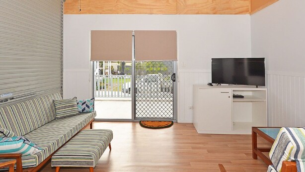 A living room with a sofa, a television on a cabinet, and a sliding glass door leading outside. - Hami's Retreat - Burrum Heads- Close to Boatramp -2BR - Aircon (Burrum Heads)