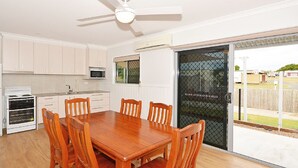 A kitchen with white cabinets, a microwave, an oven, and a dining table with chairs. - Hami's Retreat - Burrum Heads- Close to Boatramp -2BR - Aircon (Burrum Heads)