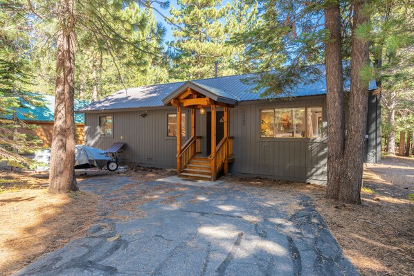 A cabin with a wooden porch, a covered driveway, and a garage.