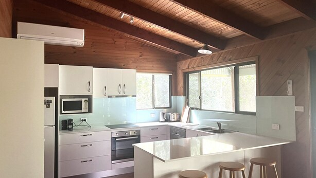 Une cuisine moderne avec des meubles blancs, un four à micro-ondes, un four traditionnel et un grand îlot central doté de tabourets.