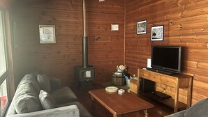 L’intérieur d’un chalet accueillant, avec un canapé, une table en bois, un téléviseur, une cheminée et des tableaux encadrés accrochés aux murs.
